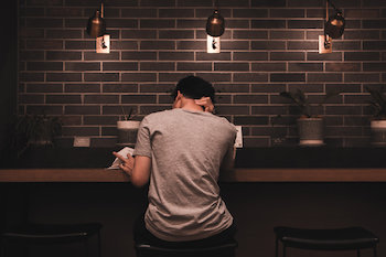 Young male sat down in a cafe reading a book holding neck in pain